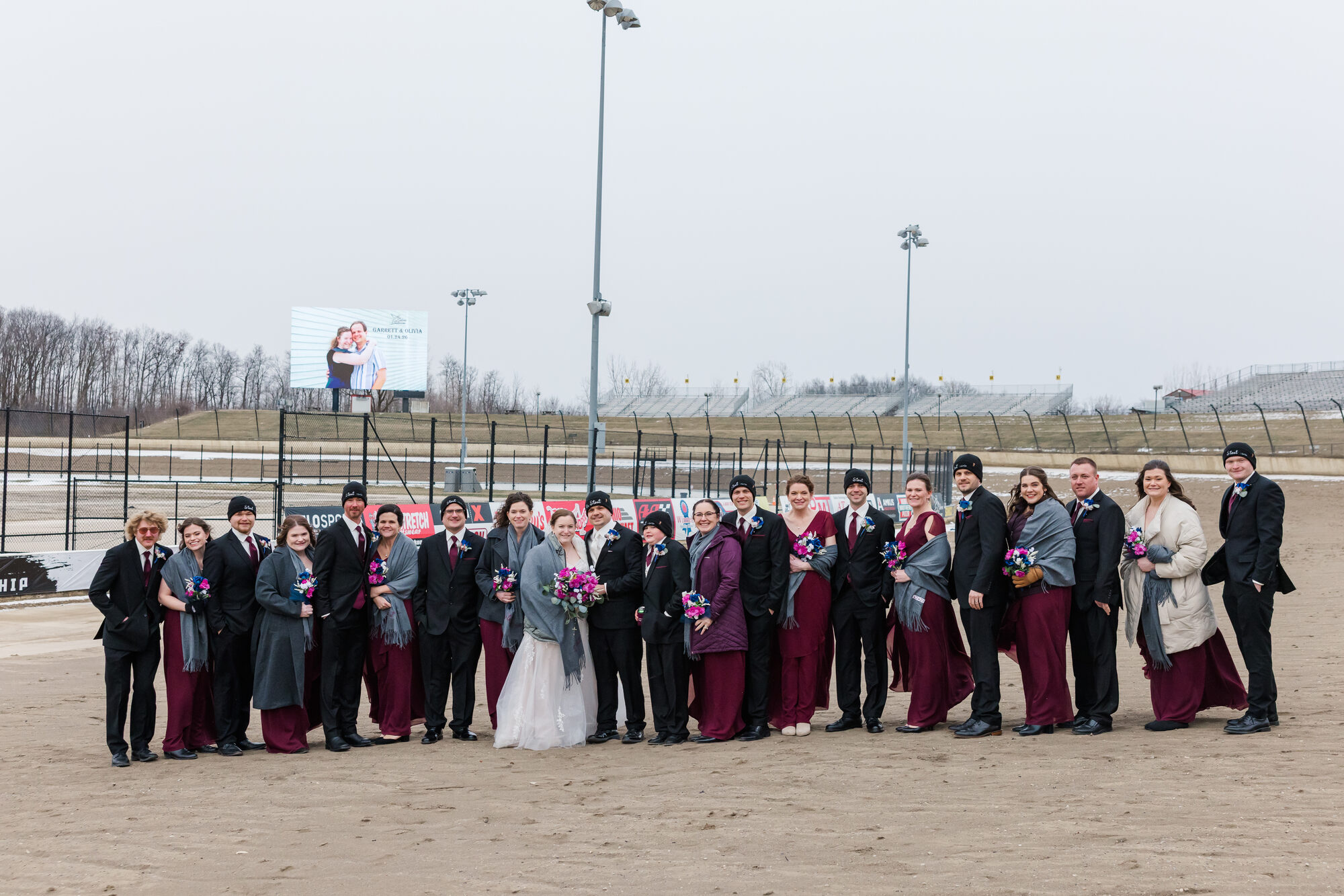 Wedding party portrait on the dirt at Eldora Speedway with the grandstands and victory screen in the background